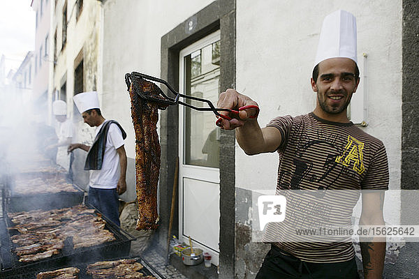 Ein junger Mann bietet Fleisch vom Grill an  der auf der Straße aufgestellt ist  Funchal  Madeira  Portugal