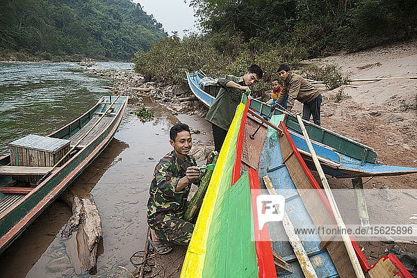 Men paint a boat on the shore of the Nam Ou River at Ban Kor Man Mai  Laos.