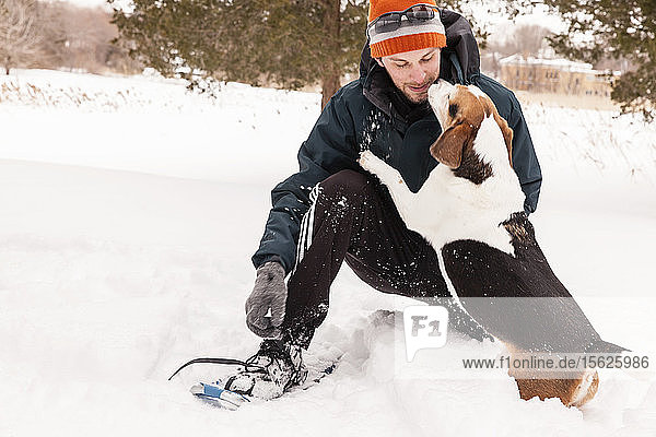 Mann beim Schneeschuhwandern mit seinem Beagle