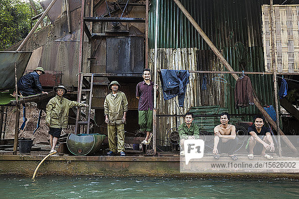 Vietnamesische und laotische Männer stehen auf dem Deck eines mechanischen Goldbaggers  der auf dem Nam Ou Fluss in Laos schwimmt.