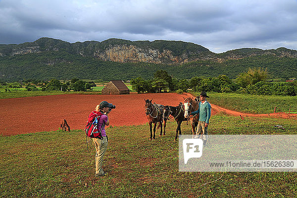 Amerikanerin fotografiert ihren Führer und ihre Pferde während eines Ausritts durch Tabakplantagen im Vinales-Tal im Westen Kubas