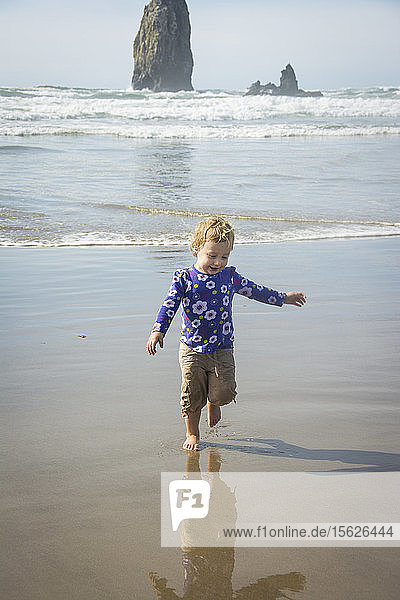 Toddler girl runs from the ocean waves on Cannon Beach  Oregon.