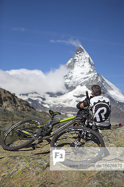 Ein Mountainbiker ruht sich aus und genießt die Aussicht auf das Matterhorn  einen berühmten Berg oberhalb von Zermatt in den Schweizer Alpen.