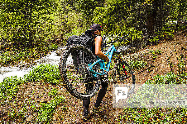 Woman in forest carries mountain bike up Ice Lakes trail  USA