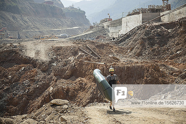 Robert Hahn carries his packraft through the original river channel - now a construction site for Dam #5 - on the Nam Ou River Laos.