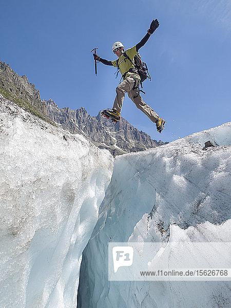 A mountain climber is jumping over a crevasse on Mer de Glace  a famous glacier in the Mont Blanc range.