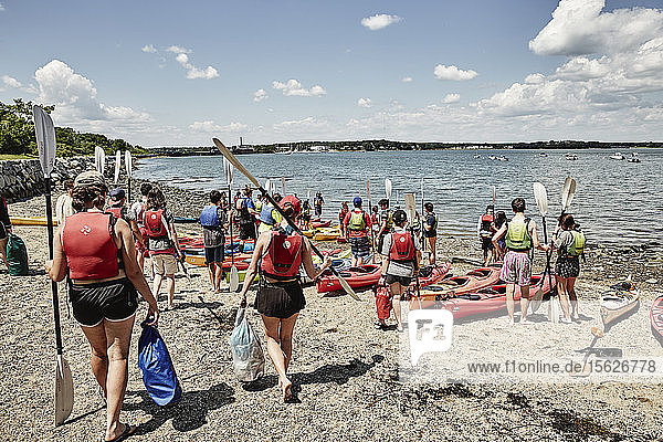 Group of people walking and standing with paddles beside kayaks lying on sea coast  Portland  Maine  USA