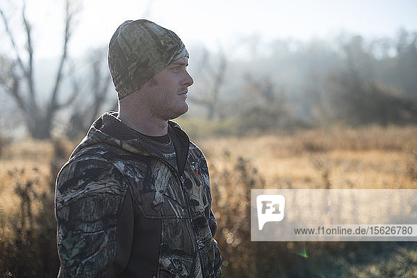 Young adult male hunter stands in field looking for deer