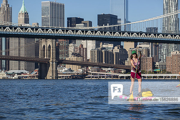 Erwachsene Frauï¾ Paddle Boardingï¾ auf East River mit Brooklyn Bridge und Stadtgebäude im Hintergrund  New York City  New York  USA