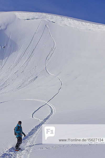 Eine Frau fährt mit ihrem Snowboard aus ihrer Linie  nachdem sie im Backcountry von Whistler von einer Felswand gesprungen ist
