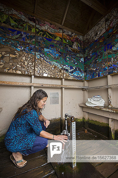Eine erwachsene Frau füllt eine wiederverwendbare Wasserflasche an einem artesischen Brunnen am Straßenrand in Ashland Wisconsin in der Nähe des Lake Superior auf.