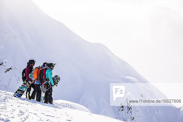 Professional snowboarders Robin Van Gyn  Helen Schettini  and Jamie Anderson  stand on a ridge and look down at a line they are about to ride on a sunny day in Haines  Alaska.