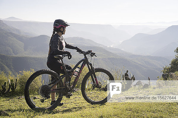 Side view of woman standing with mountain bike in natural setting with mountains in background  Pena del Aire  Huasca de Ocampo  Hidalgo  Mexico