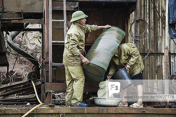 Vietnamese men empty out concentrate from the sluice box into a bag for later processing on the deck of a mechanical gold dredge floating on the Nam Ou River Laos.