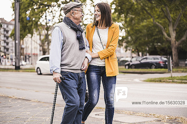 Adult granddaughter assisting her grandfather strolling with walking stick