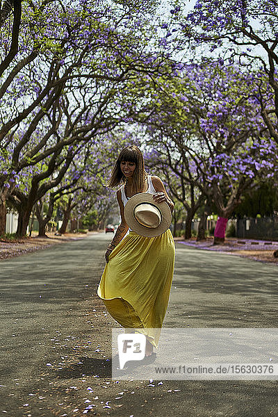 Tanzende Frau mit einem Hut auf den Händen inmitten einer Strasse voller blühender Jacaranda-Bäume Pretoria  Südafrika