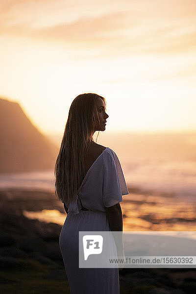 Junge Frau am Strand bei Sonnenaufgang mit seitlichem Blick