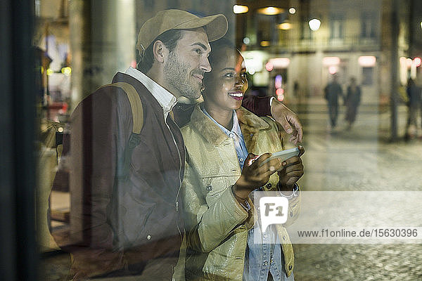 Junges Paar mit Smartphone beobachtet nachts etwas in der Stadt  Lissabon  Portugal