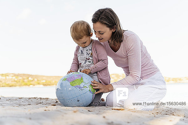 Mutter und kleine Tochter am Strand beim gemeinsamen Blick auf den Strandball der Erde