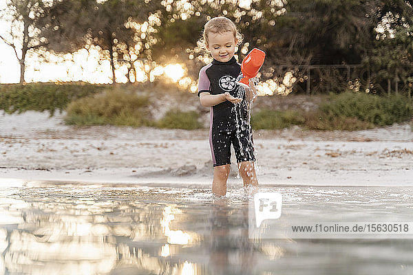 Süßes Kleinkind spielt mit Gießkanne im Meer