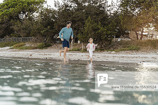 Glücklicher Vater rennt mit Tochter am Meeresufer