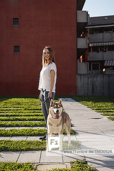 Porträt einer glücklichen jungen Frau  die abends mit ihrem Hund Gassi geht