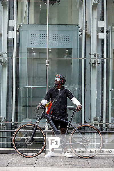 Stilvoller junger Mann mit Fahrrad und Kuriertasche in der Stadt