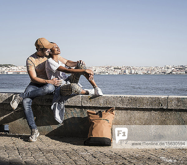 Young couple sitting on a wall at the waterfront  Lisbon  Portugal