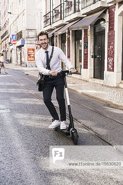 Glücklicher junger Geschäftsmann auf dem E-Scooter in der Stadt  Lissabon  Portugal