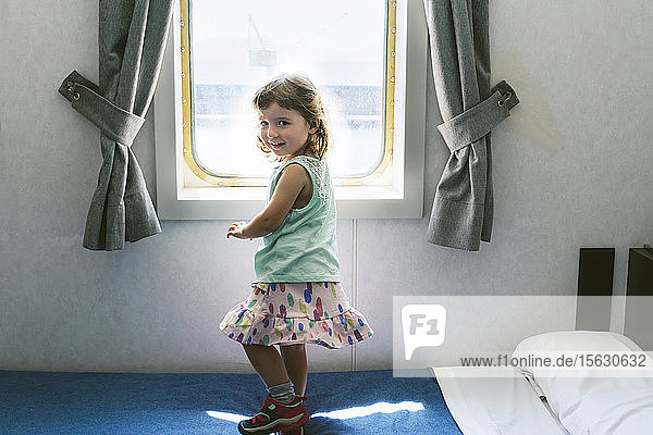 Bildnis eines kleinen Mädchens auf dem Bett der Schiffskabine vor dem Fenster stehend