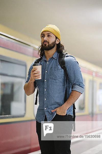 Portrait of man with backpack and coffee to go waiting at platform  Berlin  Germany