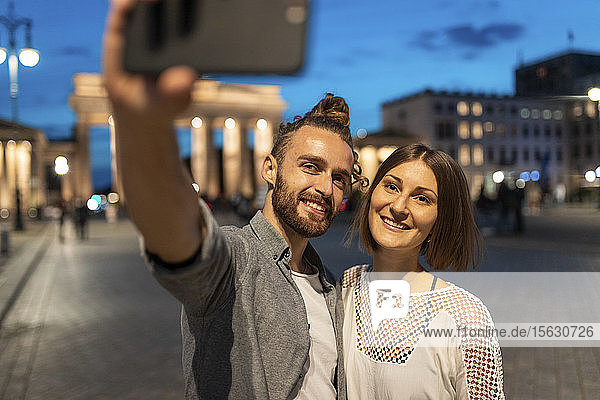 Glückliches Paar beim Selfie am Brandenburger Tor zur blauen Stunde  Berlin  Deutschland