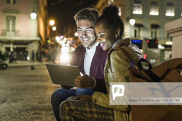 Portrait eines glücklichen jungen Paares mit digitalem Tablet in der Stadt bei Nacht Lissabon Portugal