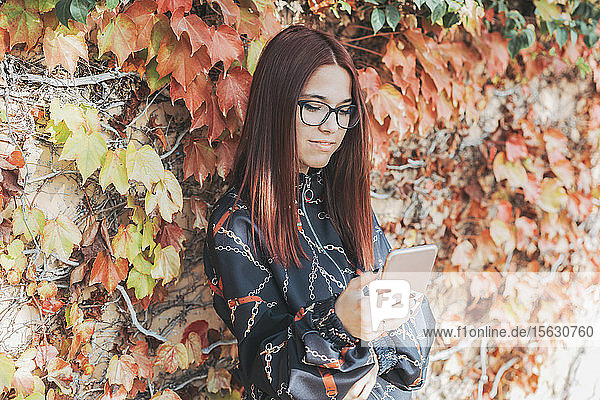 Porträt eines Teenagers mit gefärbten roten Haaren  der im Herbst sein Smartphone überprüft
