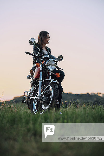 Young woman with vintage motorbike in rural scene enjoying sunset