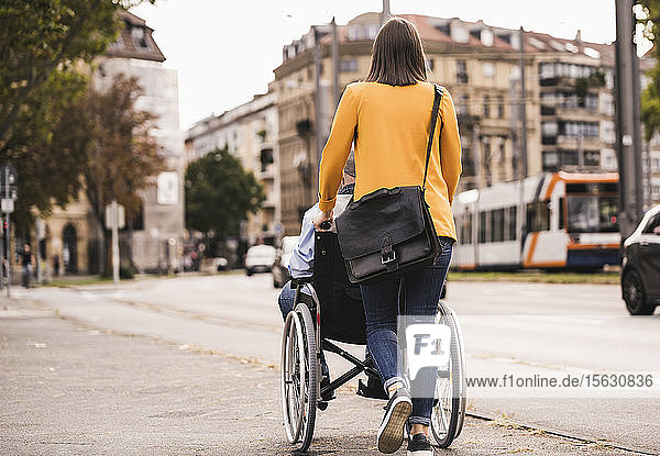 Back view of young woman pushing senior man in wheelchair