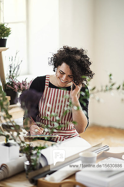 Glückliche junge Frau am Telefon in einem kleinen Laden mit Pflanzen
