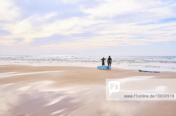 Portugal  Algarve  Silhouetten zweier Surfer  die am Strand von Cordoama stehen