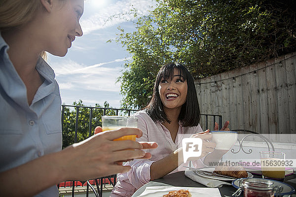 Zwei Frauen frühstücken an einem Café-Tisch im Freien  haben Spaß  unterhalten sich