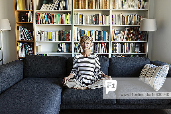 Reife Frau,  die zu Hause auf der Couch Yoga praktiziert