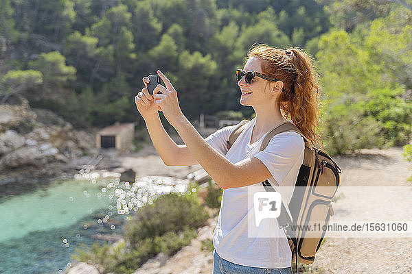 Rothaarige Frau steht auf Aussichtspunkt und fotografiert mit ihrem Smartphone