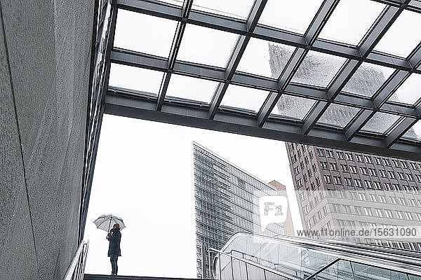 Mann mit Regenschirm telefoniert am Eingang des Bahnhofs Potsdamer Platz  Berlin  Deutschland