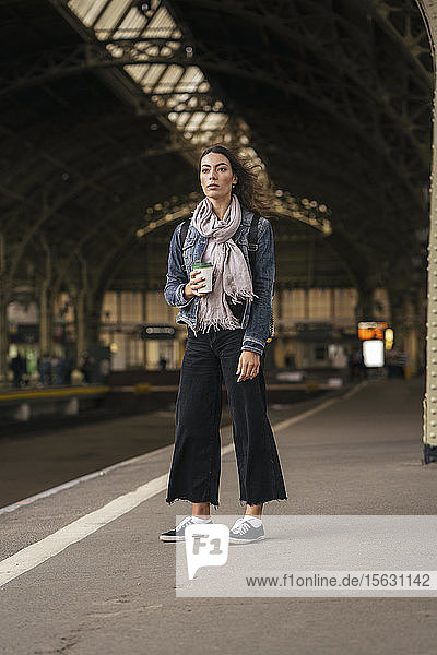 Junge weibliche Reisende steht mit Kaffee auf dem Bahnsteig
