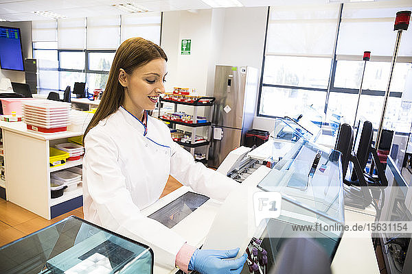 Seitenansicht einer jungen Frau im Laborkittel  die während ihrer Arbeit im Forschungslabor Fläschchen mit Blutproben in den Kühlschrank schüttet