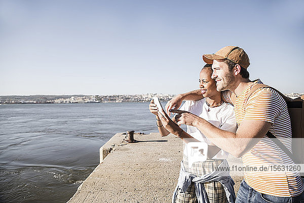 Young couple using cell phone on pier at the waterfront  Lisbon  Portugal
