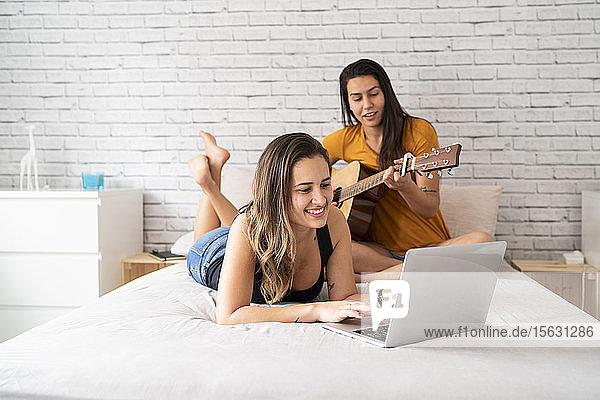 Glückliches lesbisches Paar mit Laptop und Gitarre im Bett