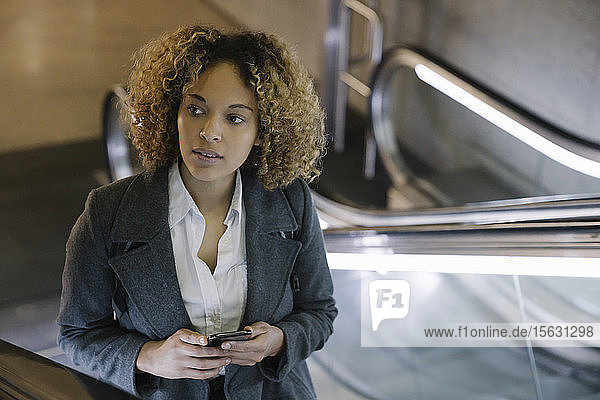 Porträt einer Frau mit Handy auf der Rolltreppe