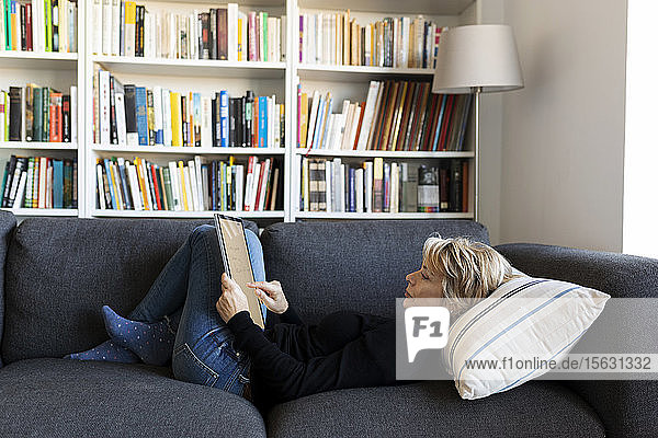 Reife Frau entspannt zu Hause auf der Couch mit Grafiktablett