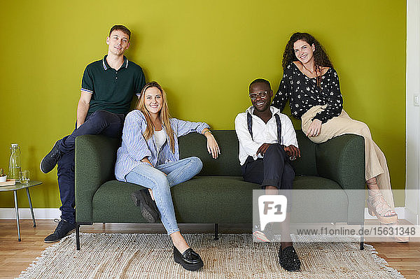 Porträt von lächelnden Kollegen  die in einer grün ummauerten Bürolounge auf einem Sofa sitzen
