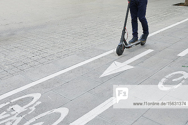 Beine eines Mannes  der auf einem E-Scooter auf dem Fahrradweg in der Stadt fährt
